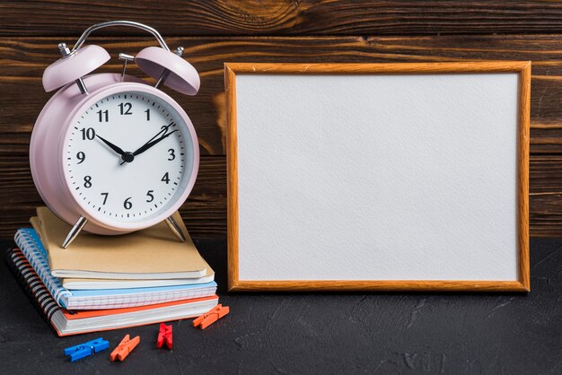 Weiße leere Tafel; Wecker; Wäscheklammer und Notizbücher auf schwarzem Schreibtisch