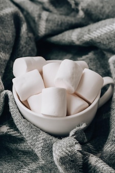 Weiße marshmallows in einer weißen tasse auf pulloverhintergrund. heißes winter-kakao-schokoladengetränk. weihnachtsbeleuchtung. gemütliche vorbereitung für urlaubsatmosphäre, aromatherapie für die kalte wintersaison. hygge