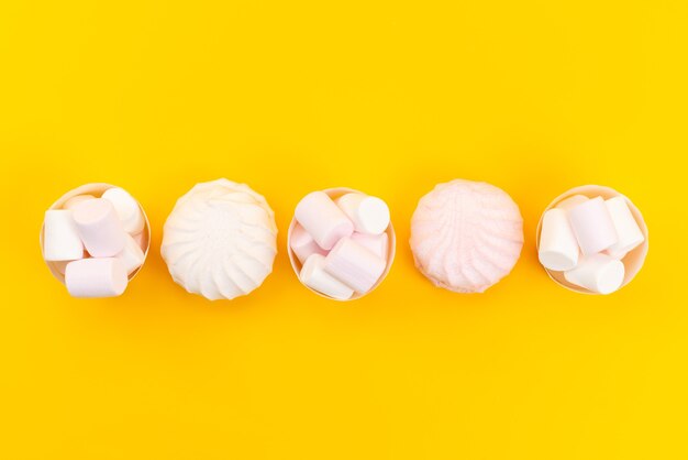 Weiße Marshmallows von oben, köstlich und lecker in Papierverpackungen auf gelbem Schreibtisch, zuckersüße Süßwaren