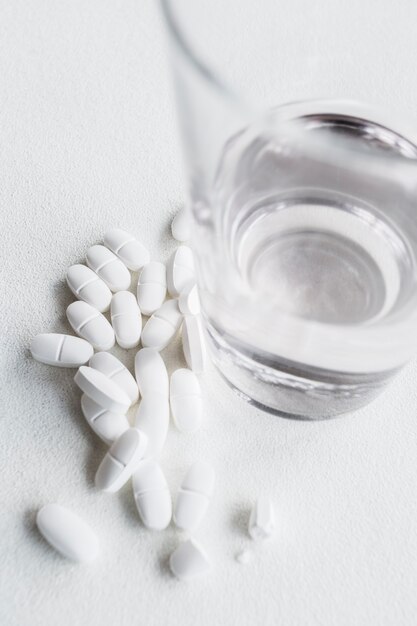 Weiße Pillen nahe einem Glas Trinkwasser