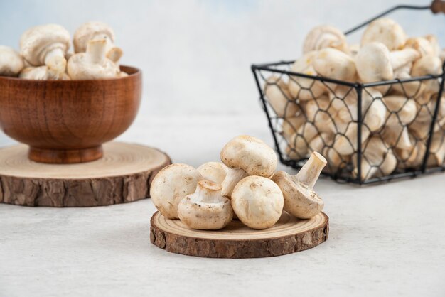 Weiße Pilze in einem metallischen Korb, in einem Holzbecher und auf einem Holzbrett.
