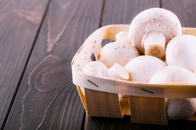 Weiße Pilze liegen auf Korb auf dunklem Holztisch