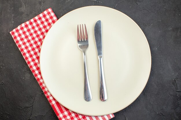 Weiße Platte von oben mit Gabel und Messer auf dunkler Oberfläche