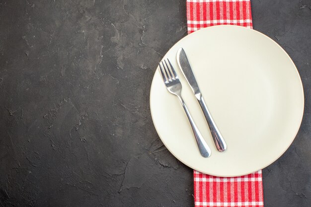 Weiße Platte von oben mit Gabel und Messer auf dunkler Oberfläche