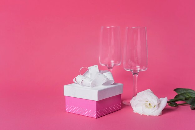 Weiße Rose; Geschenkbox und Champagnerglasgläser auf rosa Hintergrund