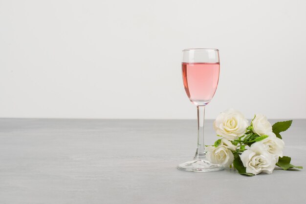 Weiße Rosen und Glas Roséwein auf grauem Tisch.