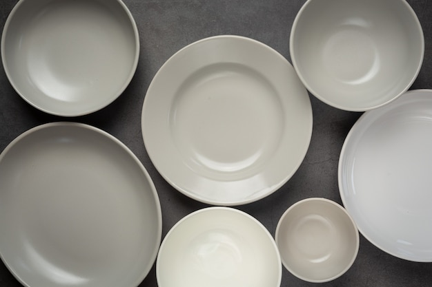 Weiße runde leere Teller und Schalen auf dunkler Oberfläche