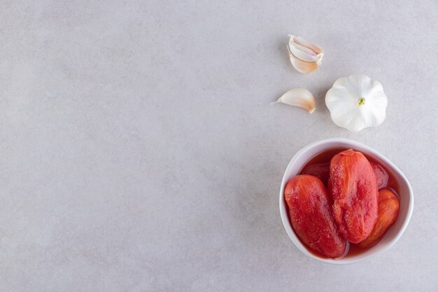 Weiße Schüssel mit eingelegten Tomaten auf Steintisch gelegt.