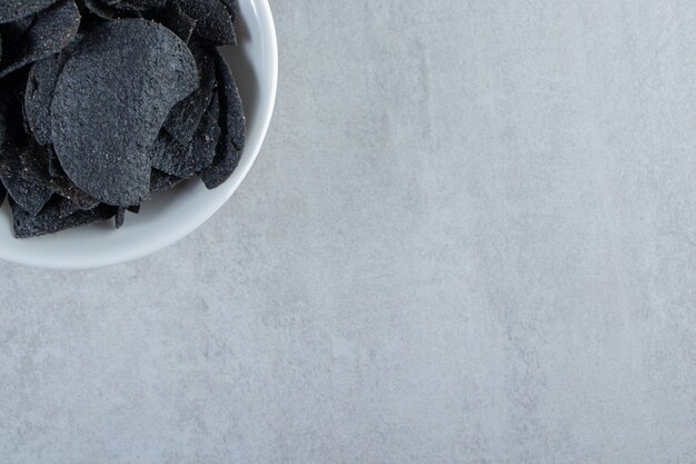 Weiße Schüssel mit gesalzenen knusprigen schwarzen Chips auf Stein.