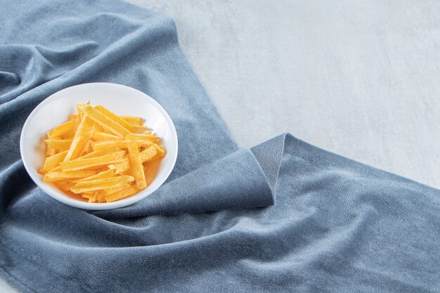 Weiße Schüssel mit knusprigen Kartoffelsticks auf blauem Tuch.