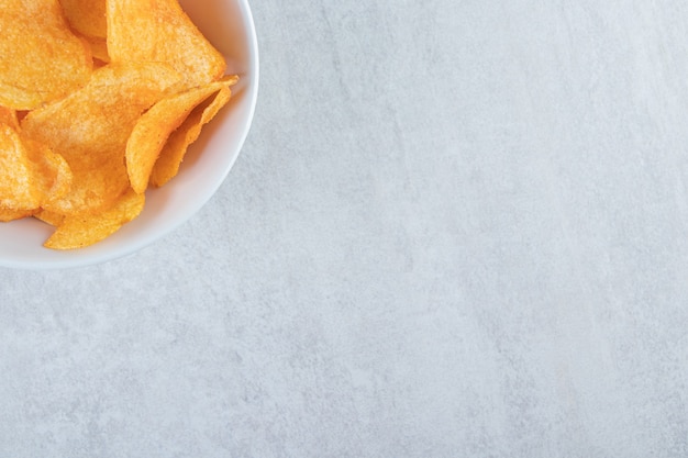 Weiße Schüssel mit leckeren Kartoffelchips auf Stein.