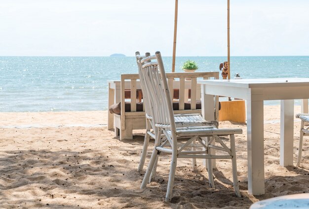 weiße Stühle und Tisch am Strand mit Blick auf blauen Ozean und klaren Himmel