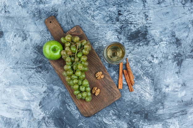 Weiße Trauben, Walnüsse, Apfel auf einem Schneidebrett mit Glas Whisky, Zimt-Draufsicht auf einem dunkelblauen Marmorhintergrund