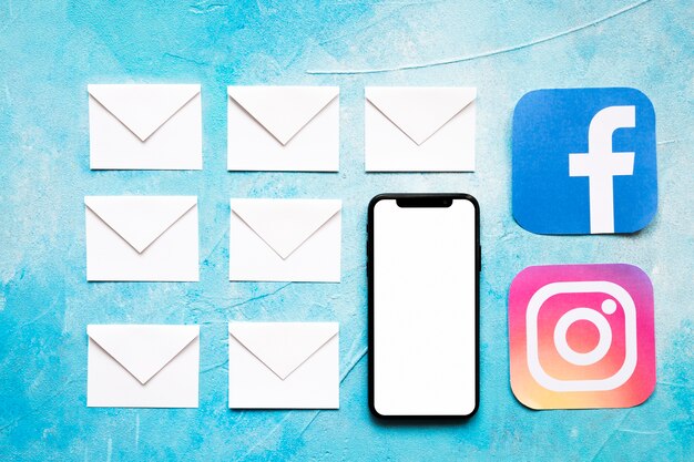 Weiße Umschlagnachrichten des Papiers und Social Media-Ikone mit Mobiltelefon auf blauem Hintergrund