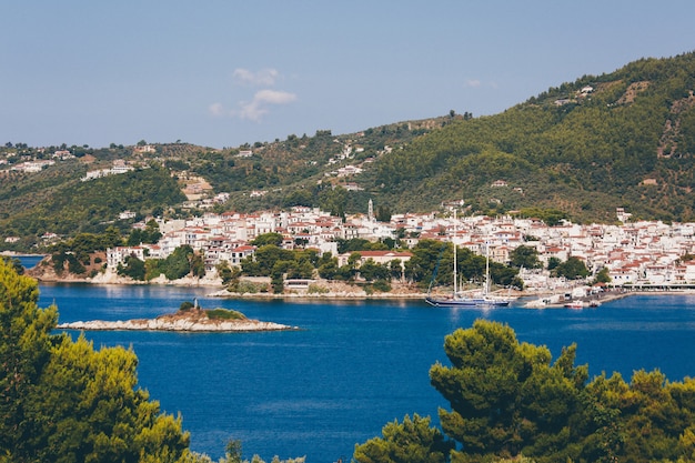 Weiße und braune Häuser in der Nähe des blauen Ozeans, umgeben von Bergen mit Bäumen in Skiathos, Griechenland