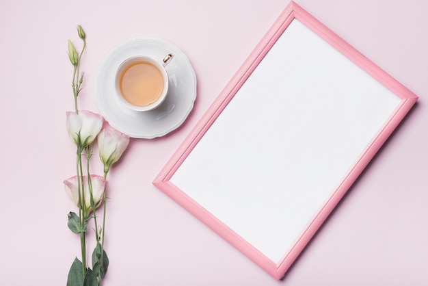 Weißer Bilderrahmen; Tasse Tee und Eustoma blüht gegen rosa Hintergrund