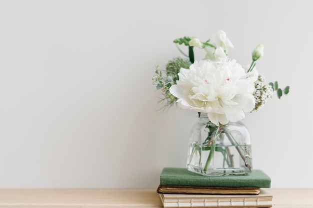Weißer Blumenstrauß in einer ausgeräumten Vase auf einem Bücherstapel