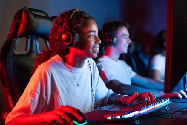 Weißer Junge und schwarzes Mädchen Teenager in Headsets spielen Videospiele in einem Videospielclub mit blauer und roter Beleuchtung Tastatur und Maus mit Beleuchten