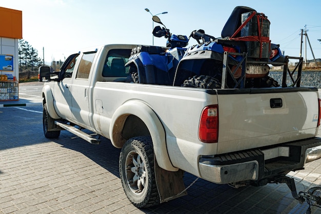 Weißer Pickup beladen mit ATV in der Nähe einer Tankstelle