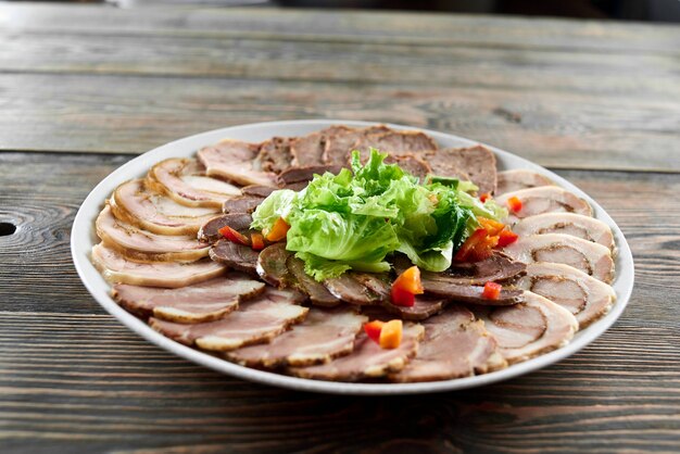 Weißer Teller auf einem Holztisch voller gefüllter Fleischsortimente, dekoriert mit frischen Salatblättern und -stücken. Leckere Vorspeise im Restaurant.