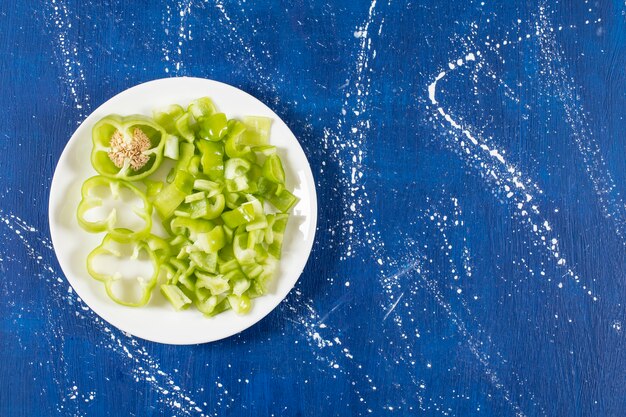 Weißer Teller gehackter grüner Paprika auf Marmoroberfläche.