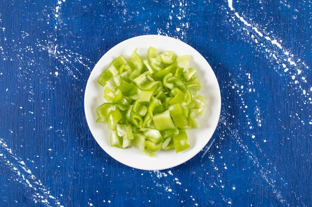 Kostenloses Foto weißer teller mit in scheiben geschnittenen grünen paprika auf marmortisch.