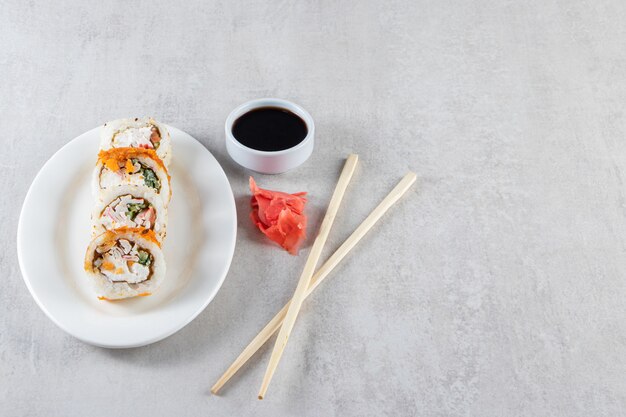 Weißer Teller mit Sushirollen und Sojasauce auf Steinhintergrund.