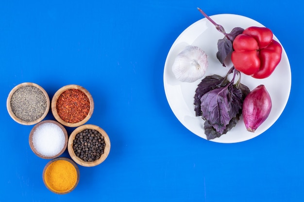 Weißer Teller mit Tomaten, Knoblauch und Zwiebeln auf blauer Oberfläche.