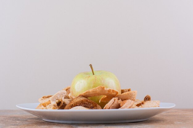 Weißer Teller mit trockenen Apfelringen und frischem grünem Apfel auf Marmortisch. Hochwertiges Foto
