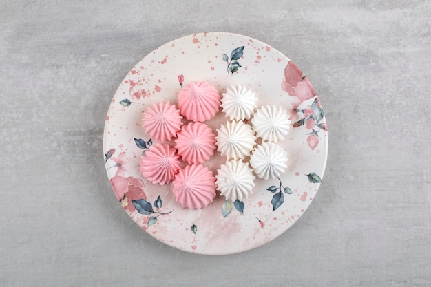 Weißer Teller mit weißen und rosa Baisersüßigkeiten auf Steintisch.