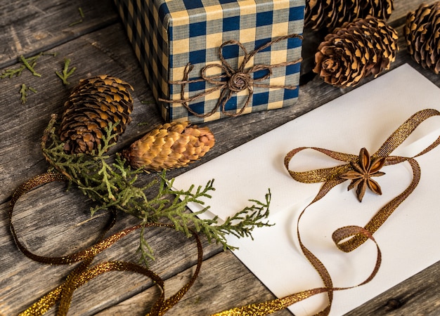 Weißer Umschlag auf Holzwand mit Tannenzapfen und Weihnachtsgeschenk