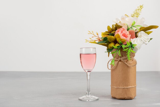 Weißer und rosa Rosenstrauß und Glas Roséwein auf grauem Tisch