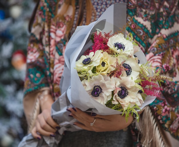 Weißer Windblumenblumenstrauß in den Händen einer Frau im soho Schal