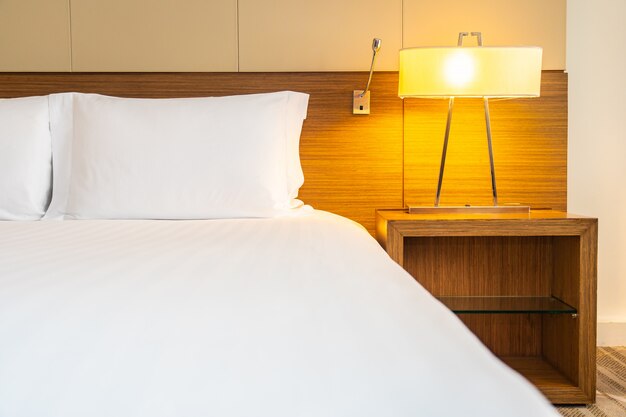 Weißes bequemes Kissen und Decke auf Bett mit Lichtlampe