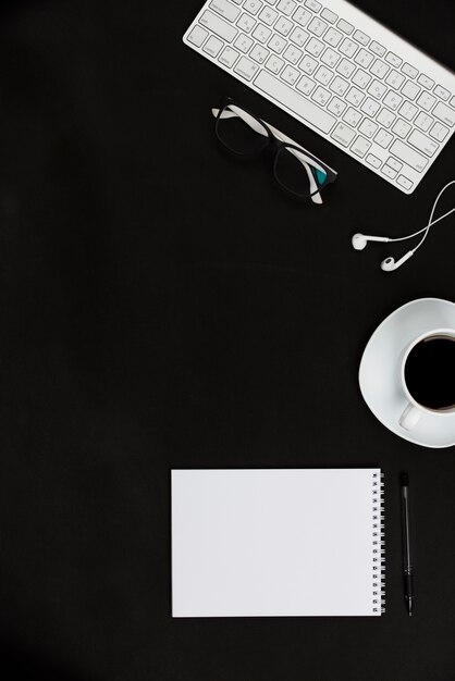Weißes Büroartikel und Kaffeetasse auf schwarzem Desktop