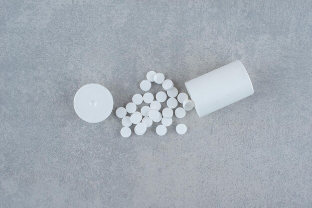 Weißes Glas mit Medikamenten auf Grau