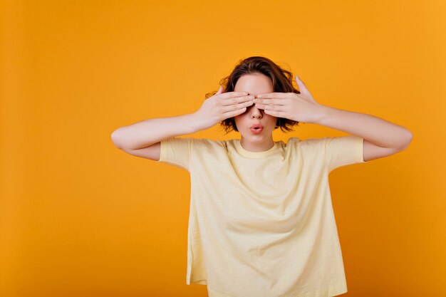 Weißes kurzhaariges Mädchen trägt Ringspiele im Versteckspiel. Innenfoto der brünetten Dame im übergroßen T-Shirt, das Augen bedeckt.