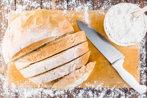 Weißes Mehl verbreitete sich über dem Brotlaib mit Messer auf Schneidebrett