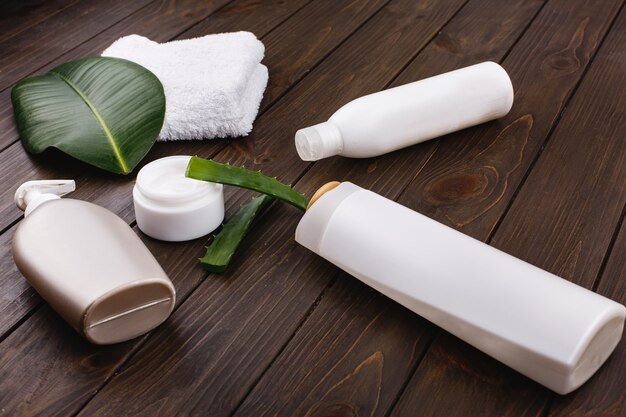 Weißes Tuch, Flaschen Shampoo und Conditioner liegen auf einem Tisch mit grünem Blatt und Aloe
