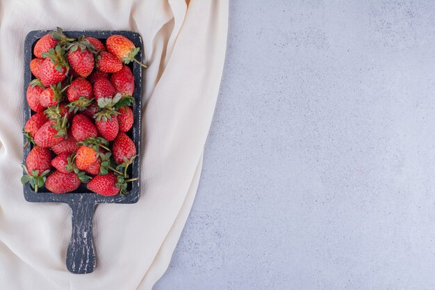 Weißes Tuch unter einem Tablett mit gestapelten Erdbeeren auf Marmorhintergrund. Foto in hoher Qualität