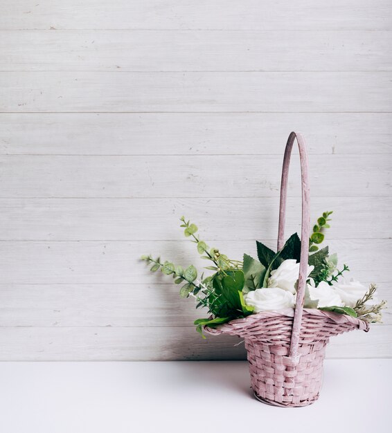 Weißrosenblumenblumenstrauß auf weißem Schreibtisch gegen hölzerne Wand