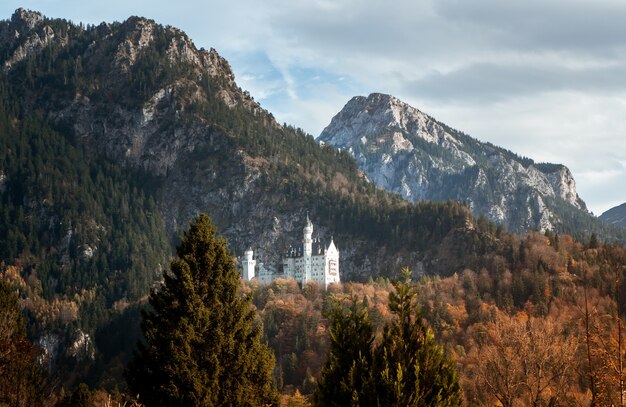 Weitwinkelaufnahme des Schlosses Neuschwanstein in Deutschland hinter einem vom Wald umgebenen Berg