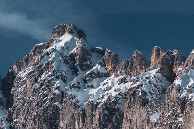 Weitwinkelaufnahme einer großen Bergformation mit Schnee, der einige Teile davon bedeckt, und einem blauen Himmel