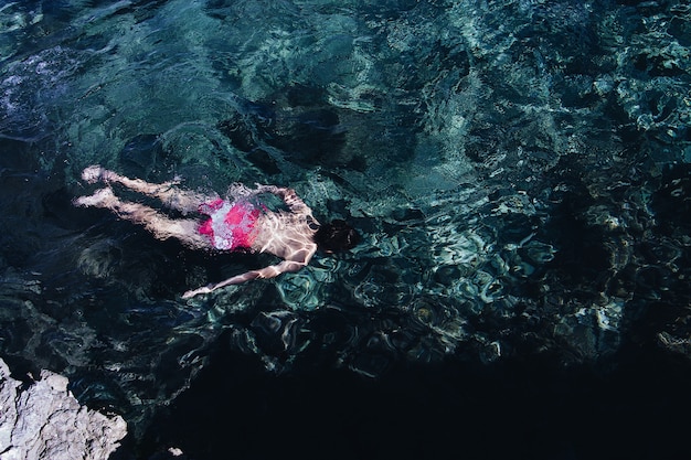 Weitwinkelaufnahme einer Person, die rosa und weißen Badeanzug trägt, der in einem klaren Meer schwimmt