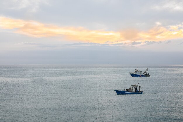 Weitwinkelaufnahme von zwei Schiffen, die unter einem bewölkten Himmel über den Ozean segeln