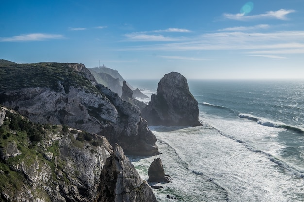 Wellen des Ozeans krachen unter dem blauen Himmel in die felsige Küste