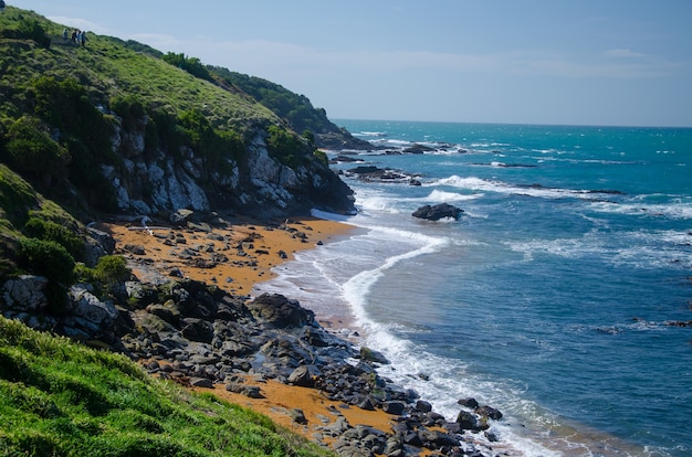 Wellenförmiger Ozean, der den felsigen Strand trifft, der durch Klippen in Neuseeland umgeben ist