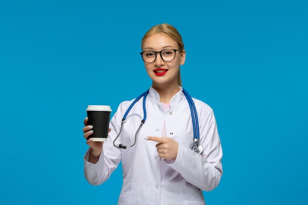 Weltärztetag süßer blonder arzt, der kaffeetasse mit dem stethoskop im medizinischen mantel hält