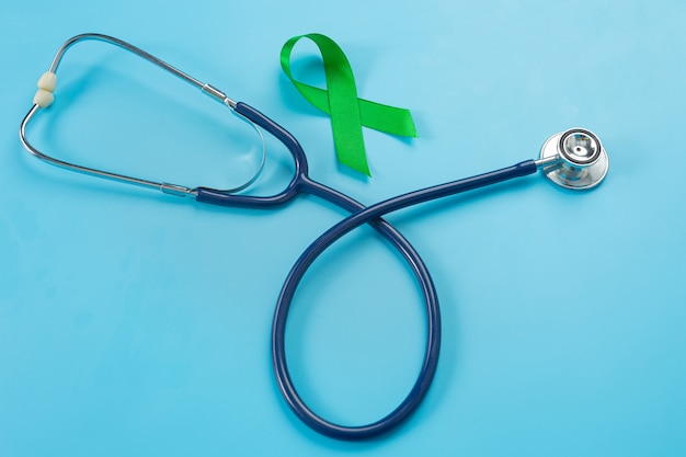 Welttag der psychischen Gesundheit, grünes Band und Stethoskop auf blauem Hintergrund