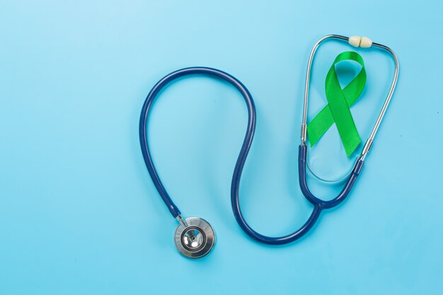 Welttag der psychischen Gesundheit, grünes Band und Stethoskop auf blauem Hintergrund